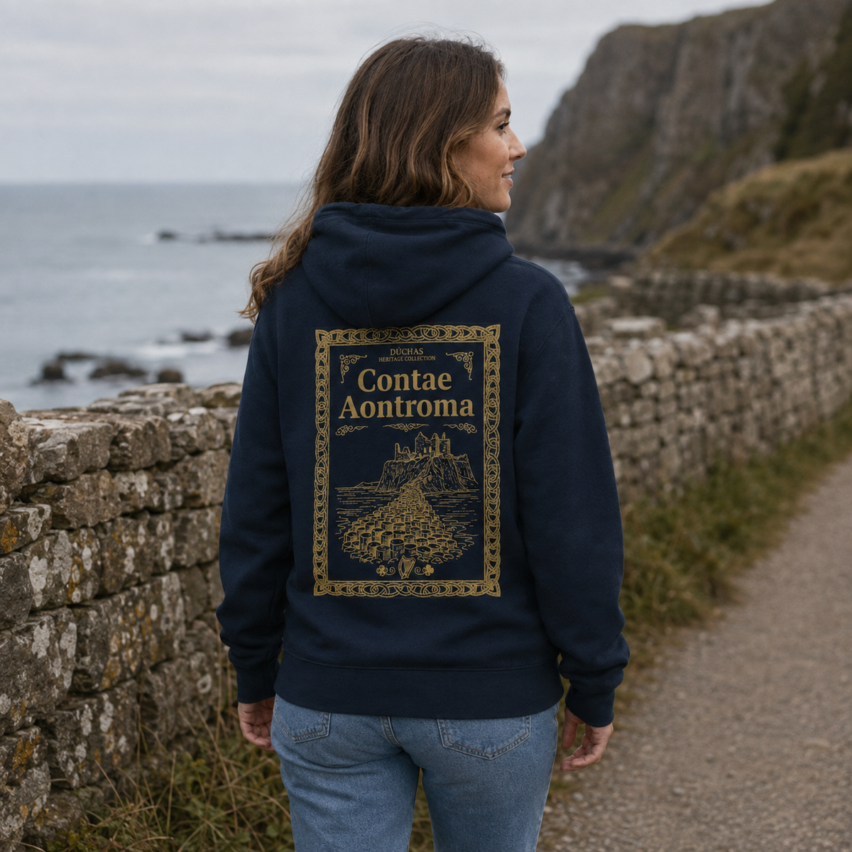 Woman wearing the navy Antrim Heritage Hoodie from the back on a quiet coastal path