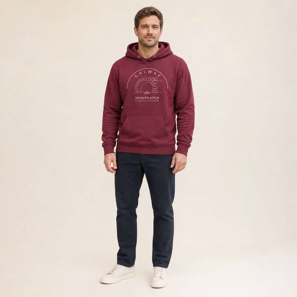 A man modeling a maroon pullover hoodie with a white graphic print on the chest, paired with dark navy pants and white sneakers, against a solid light beige background.